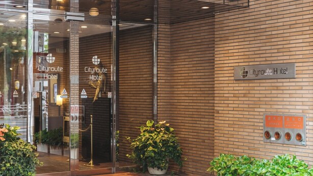 Exterior del Hotel Cityroute, con fachada de ladrillo, entrada de vidrio y plantas en macetas.