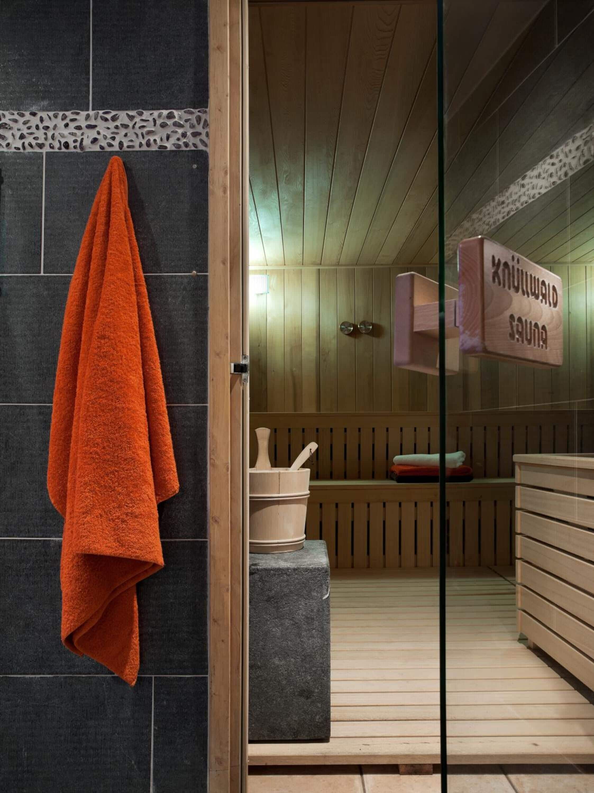 Un sauna con bancos de madera, un banco de piedra y un perchero con una toalla naranja.
