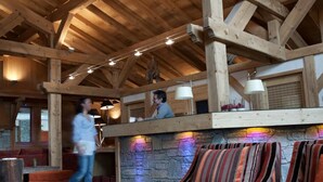 Um interior rústico com vigas de madeira aparentes, parede de pedra e assentos estofados com padrão listrado.