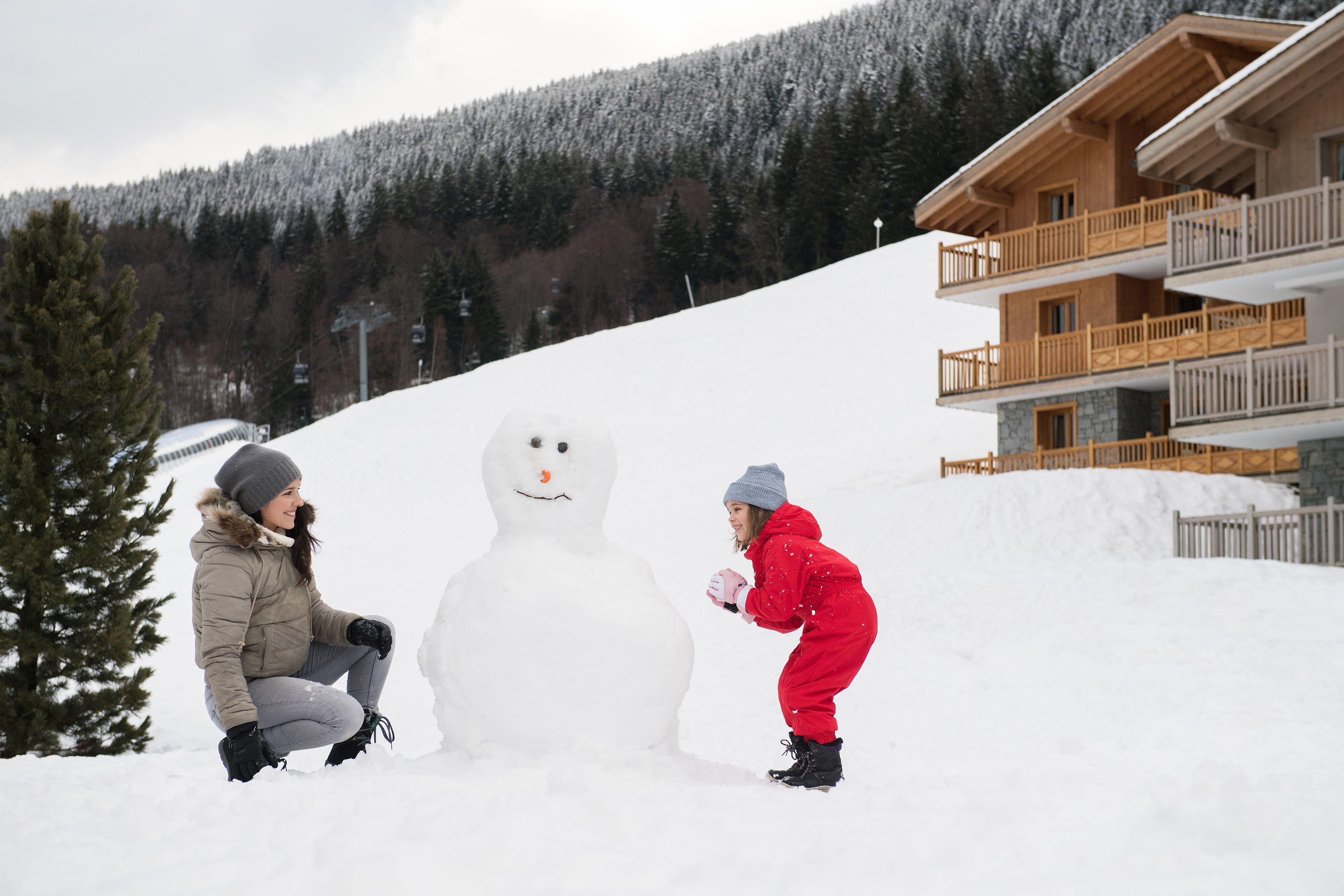 A snowman with two people in winter clothing.