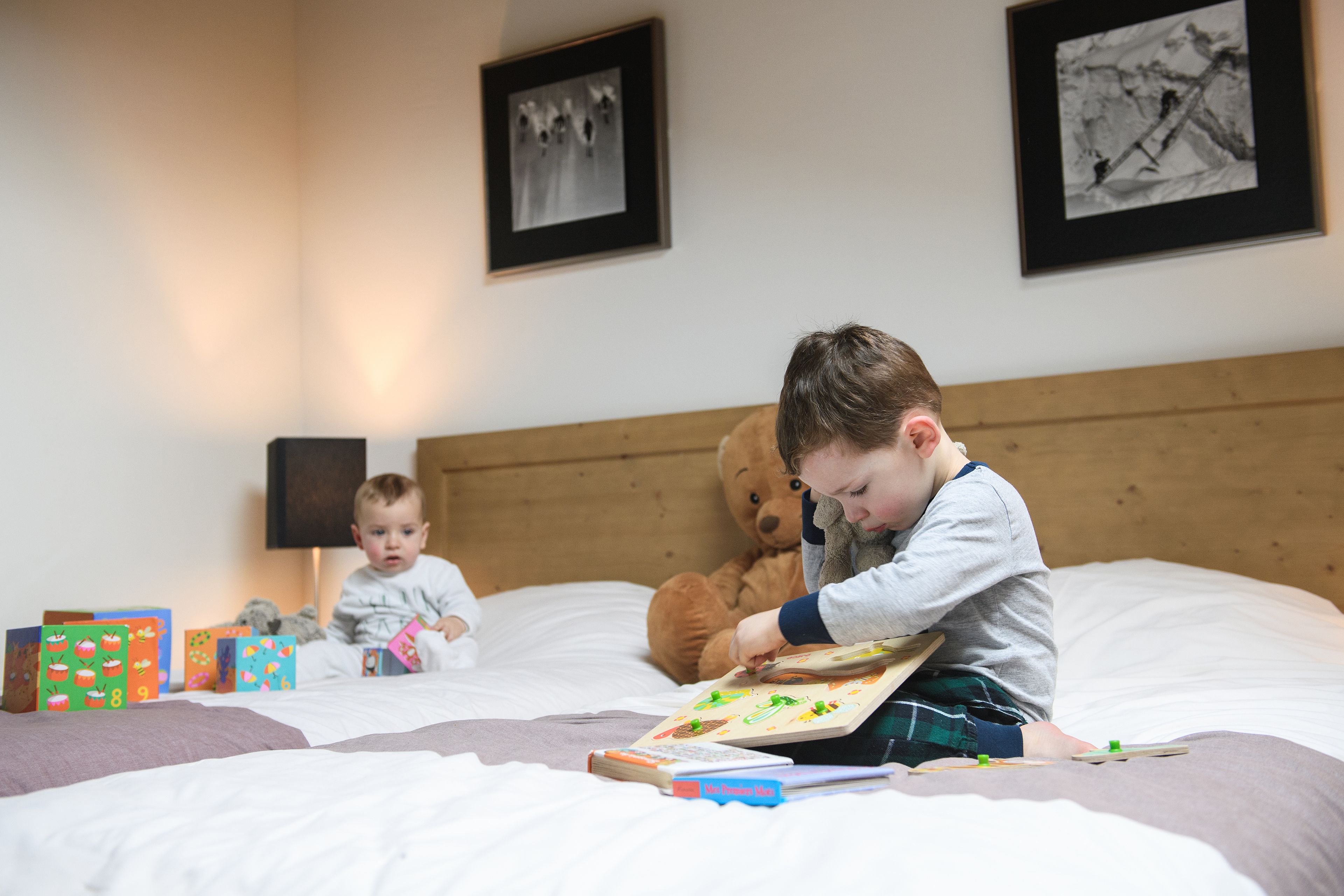 A child sitting on a bed with a book and a teddy bear, surrounded by colorful toys and books.