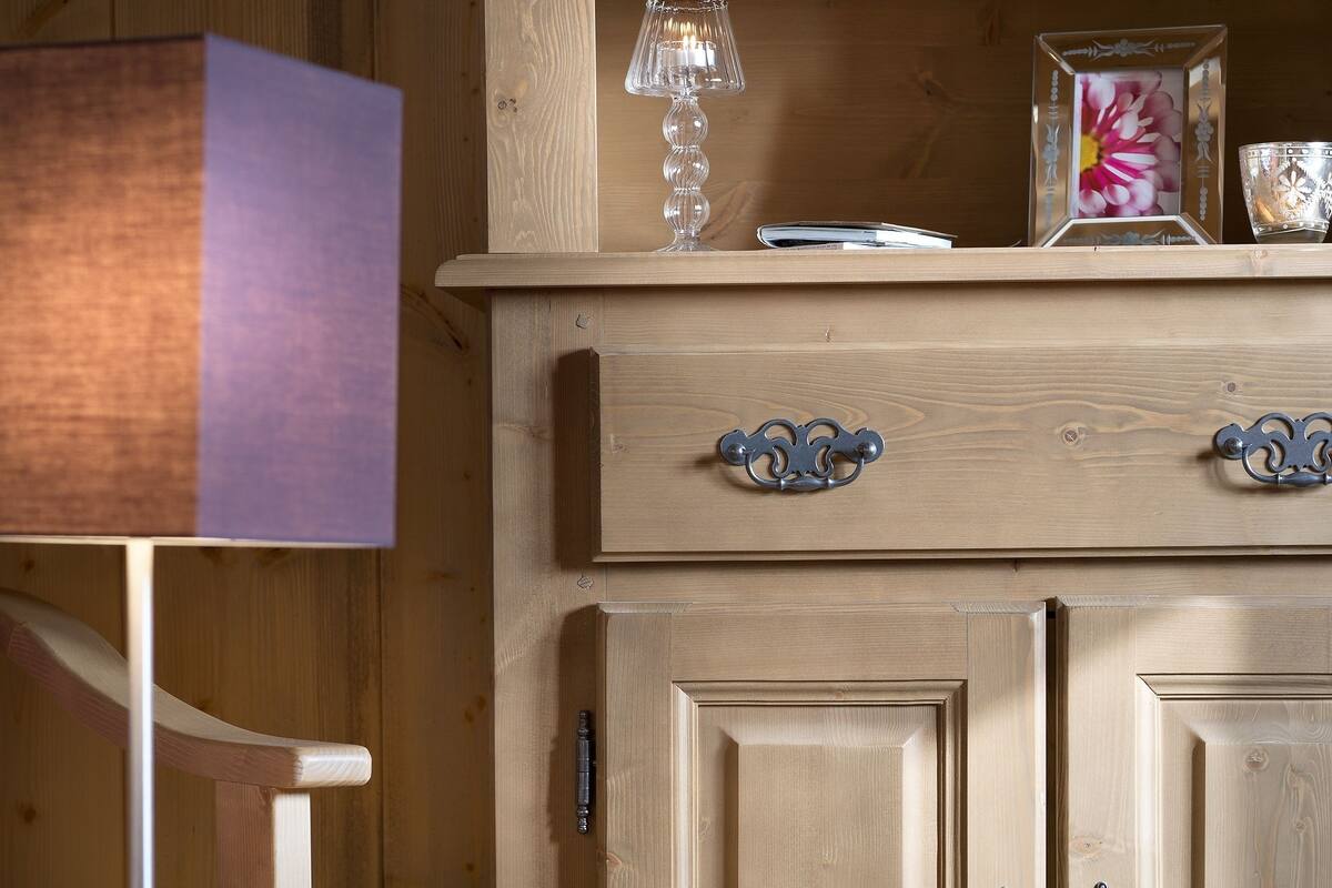 Un mueble de madera con tiradores decorativos, un vaso encima y un cuadro enmarcado.