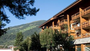 Un immeuble en bois à plusieurs étages, doté de balcons, qui se dresse sur un fond de paysage montagneux.