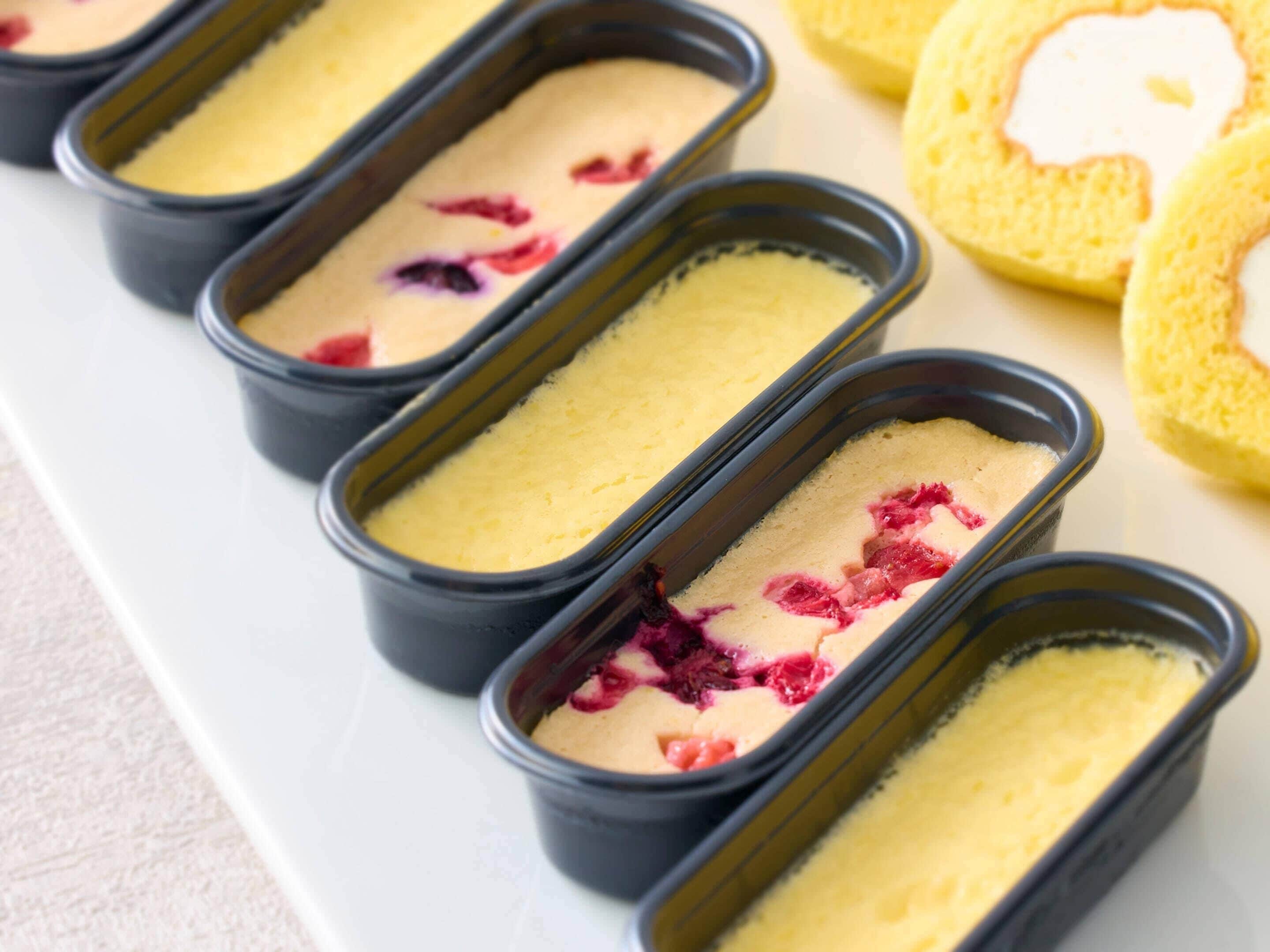 Un plateau rempli de petites coupes de dessert, chacune garnie d’une crème onctueuse et de morceaux de fruits rouges, ainsi qu’une assiette de tranches de gâteau éponge.