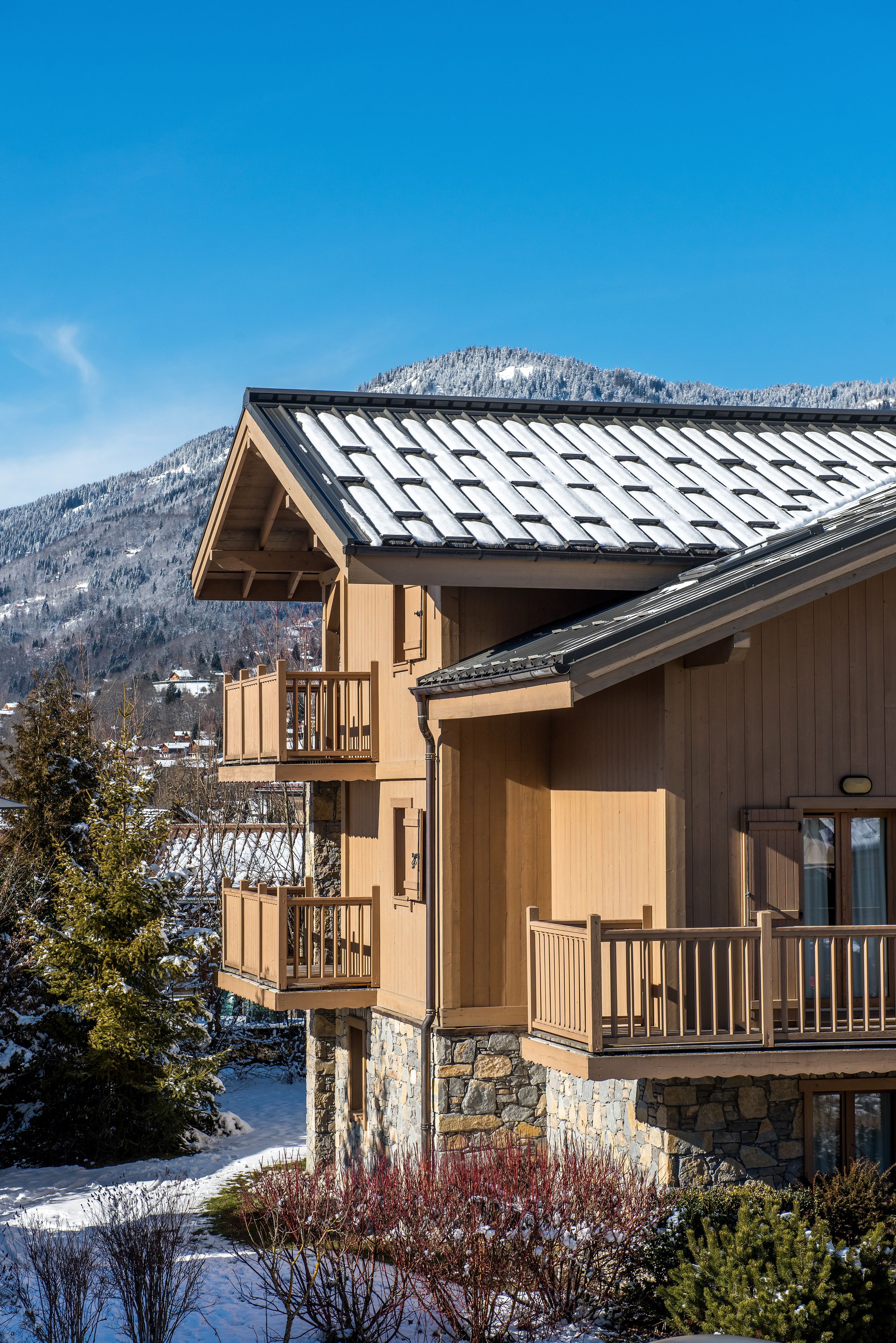 A two-story wooden building with a stone foundation, a balcony on the upper floor, and a view of a snowy mountain range.