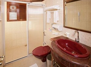 A bathroom with a glass door shower, a red sink, and a mirror above the sink.
