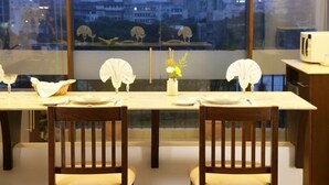 A dining table set for two with a view of city buildings through a window. - Perfect Haven Egmore Serviced Apartments (Chennai)