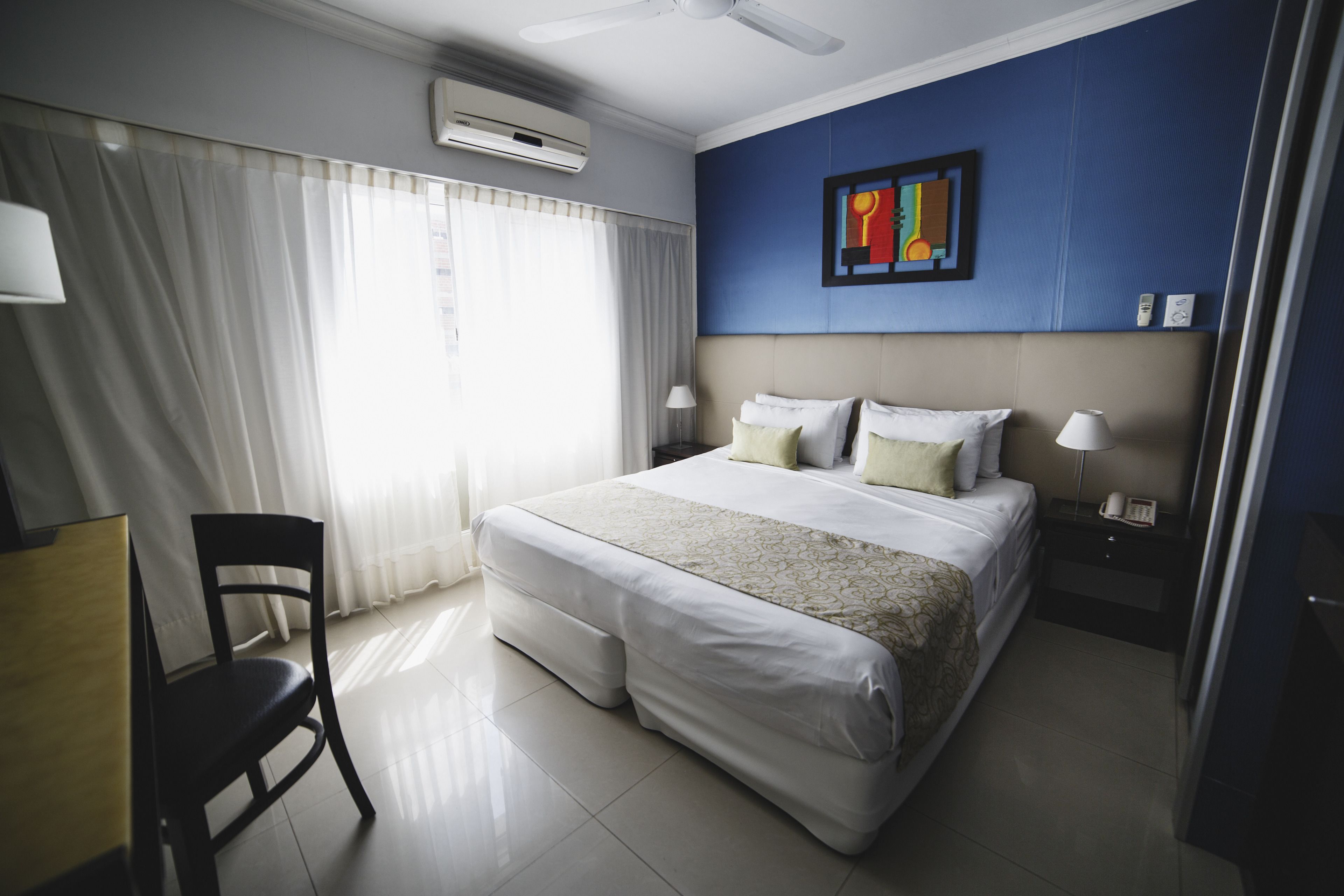Una habitación de hotel con una cama, una silla, un escritorio, una mesita de noche y un aire acondicionado instalado en la pared.