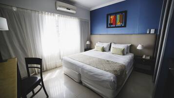 Una habitación de hotel con una cama, una silla, un escritorio, una mesita de noche y un aire acondicionado instalado en la pared.