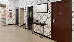 Een moderne hotellobby met een patroonmuur, een receptiebalie, een lift en een houten deur.