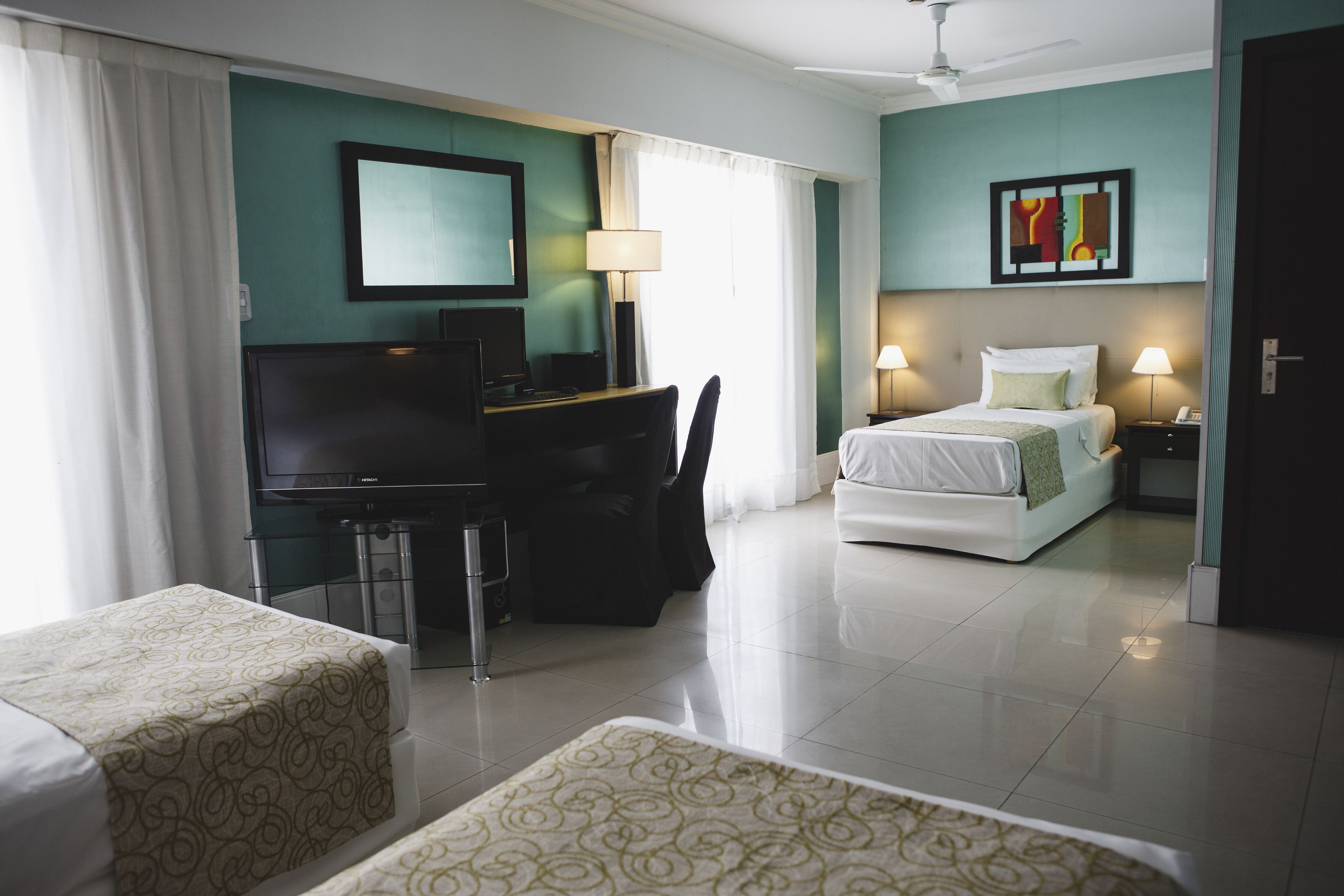 Habitación de hotel con una cama, un escritorio con computadora, un televisor y dos lámparas de noche.