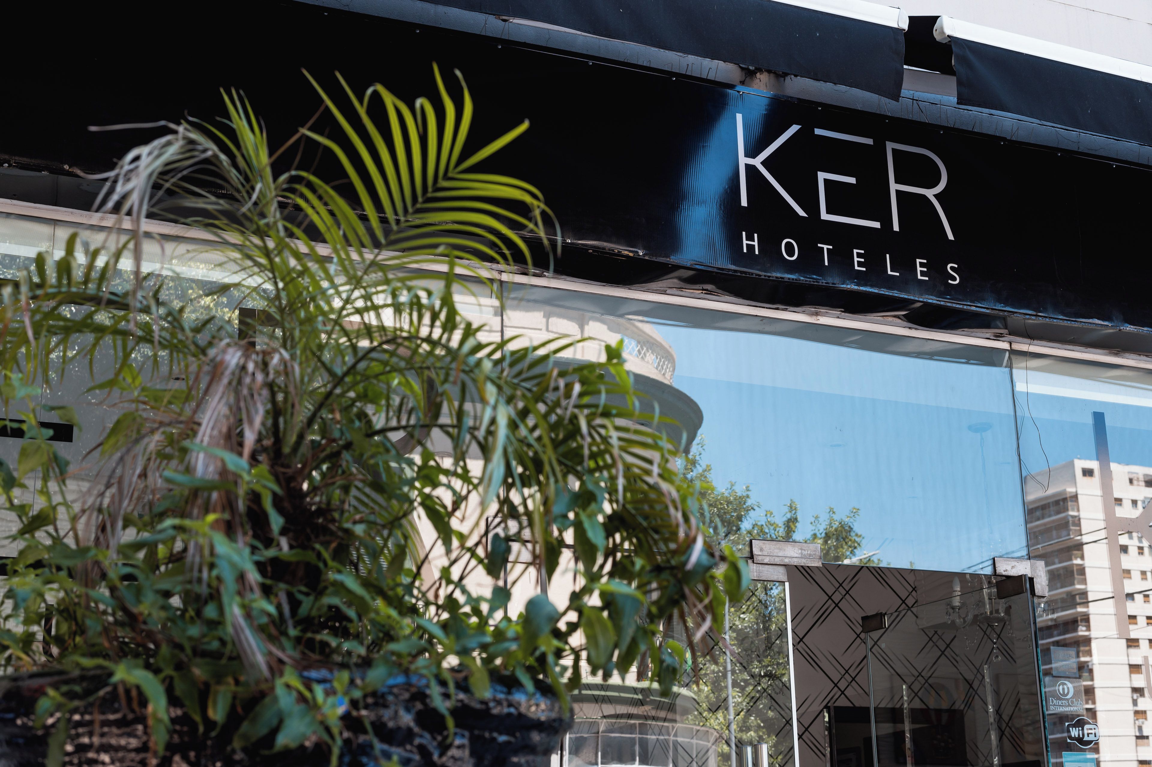 Un letrero de hotel con el nombre "KER HOTELES" y un edificio moderno al fondo.