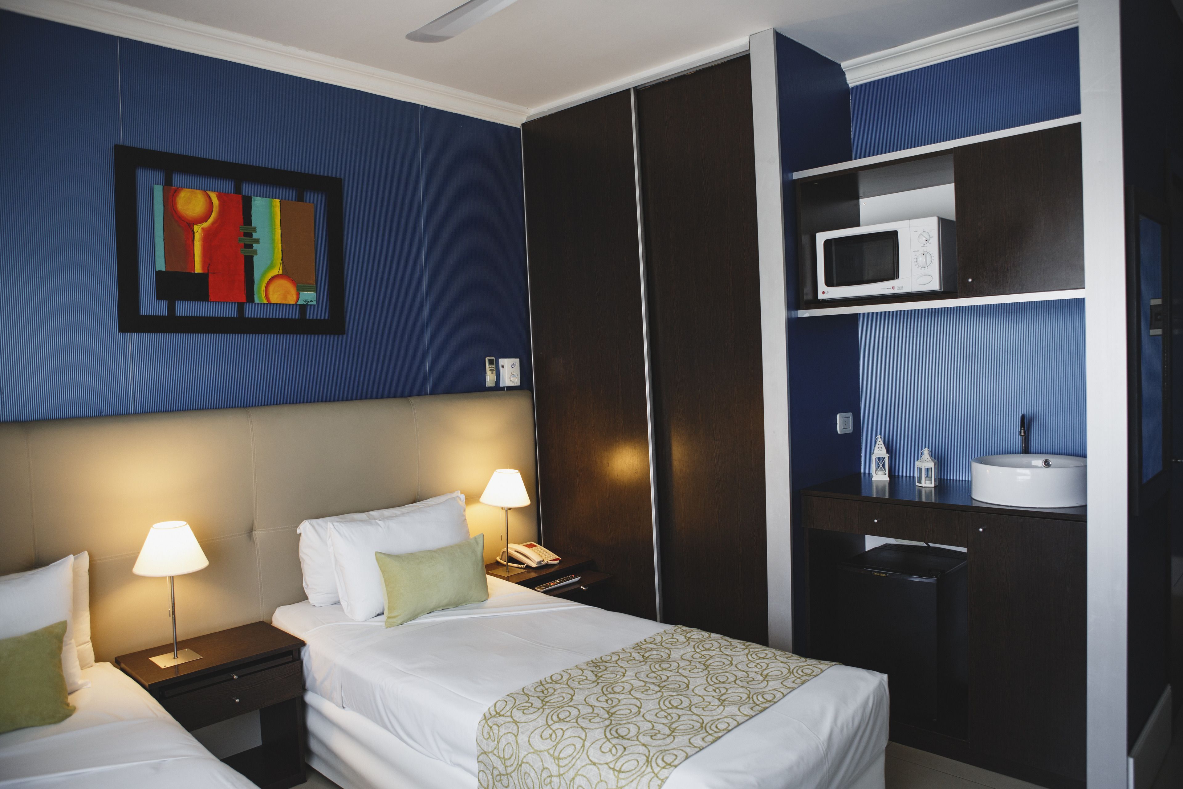 A hotel room with a bed, bedside lamps, a nightstand, a wardrobe, a microwave, and a sink.