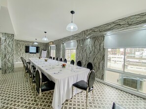 A conference room with a long table, chairs, a TV screen, and a large window.