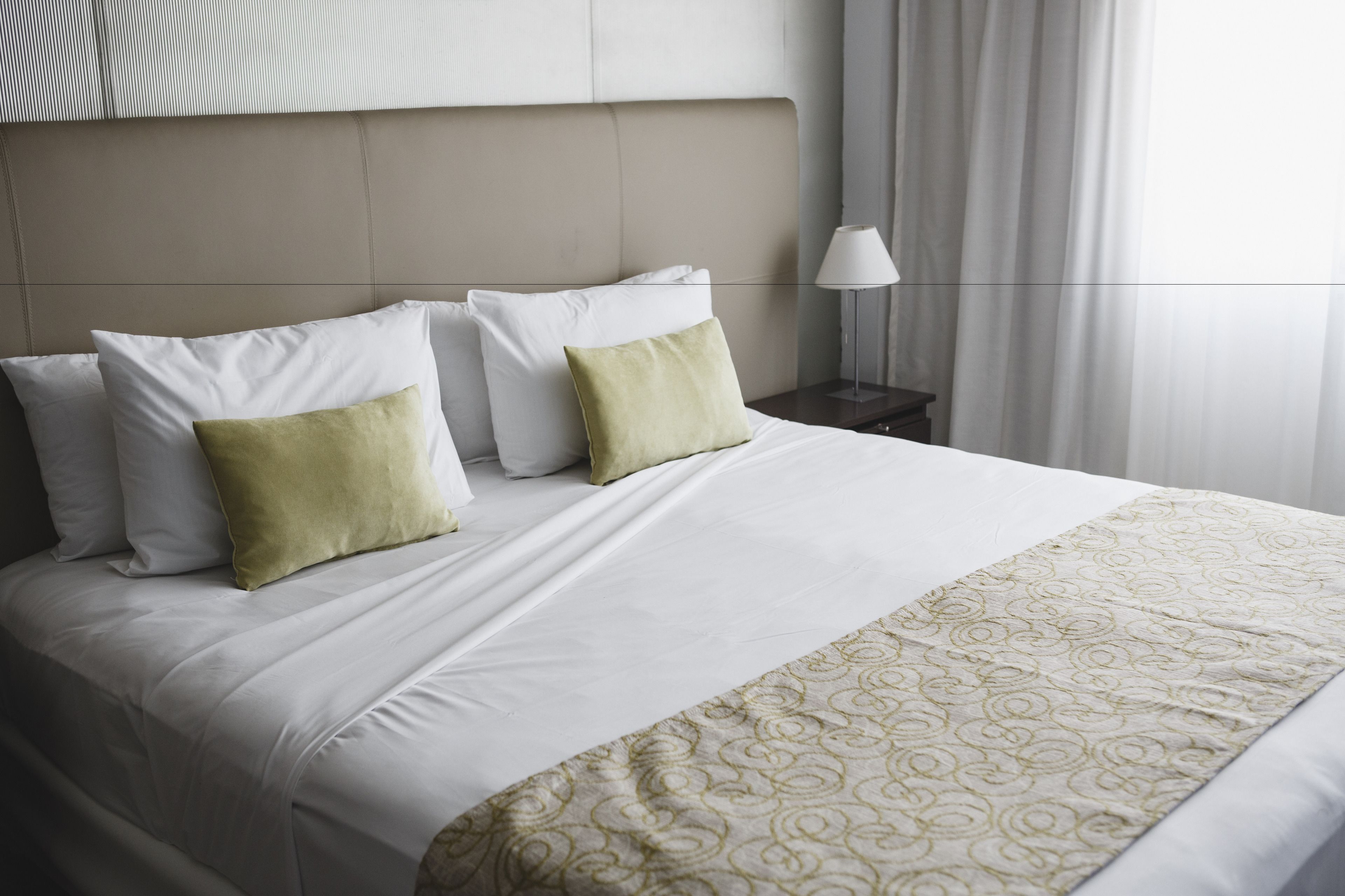 A neatly made bed with white and green pillows, a patterned throw, and a bedside table with a lamp.