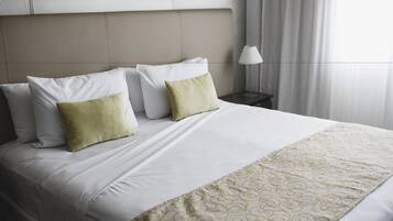 A neatly made bed with white and green pillows, a patterned throw, and a bedside table with a lamp.