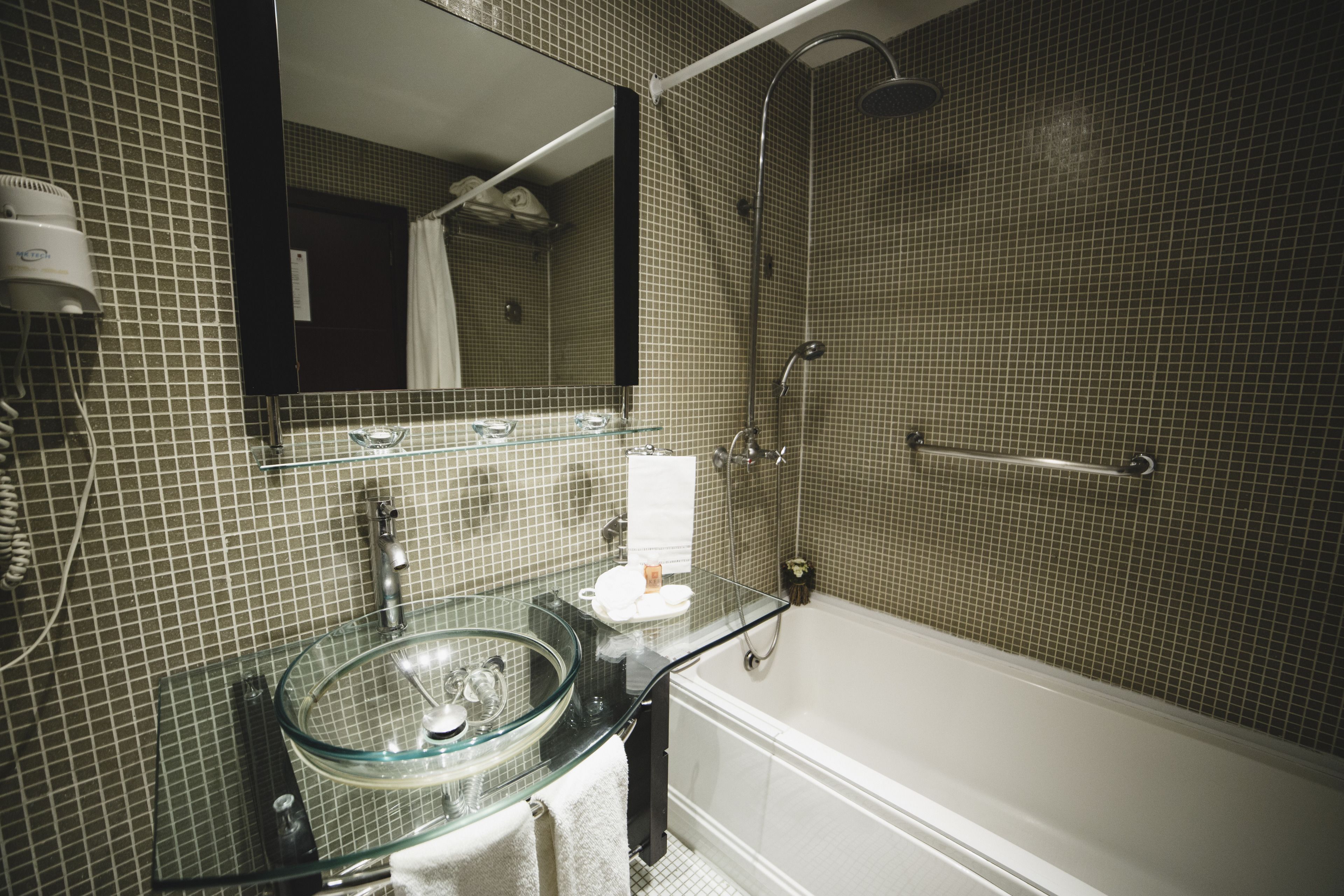 Un baño con lavamanos de vidrio, un espejo, ducha y bañera.