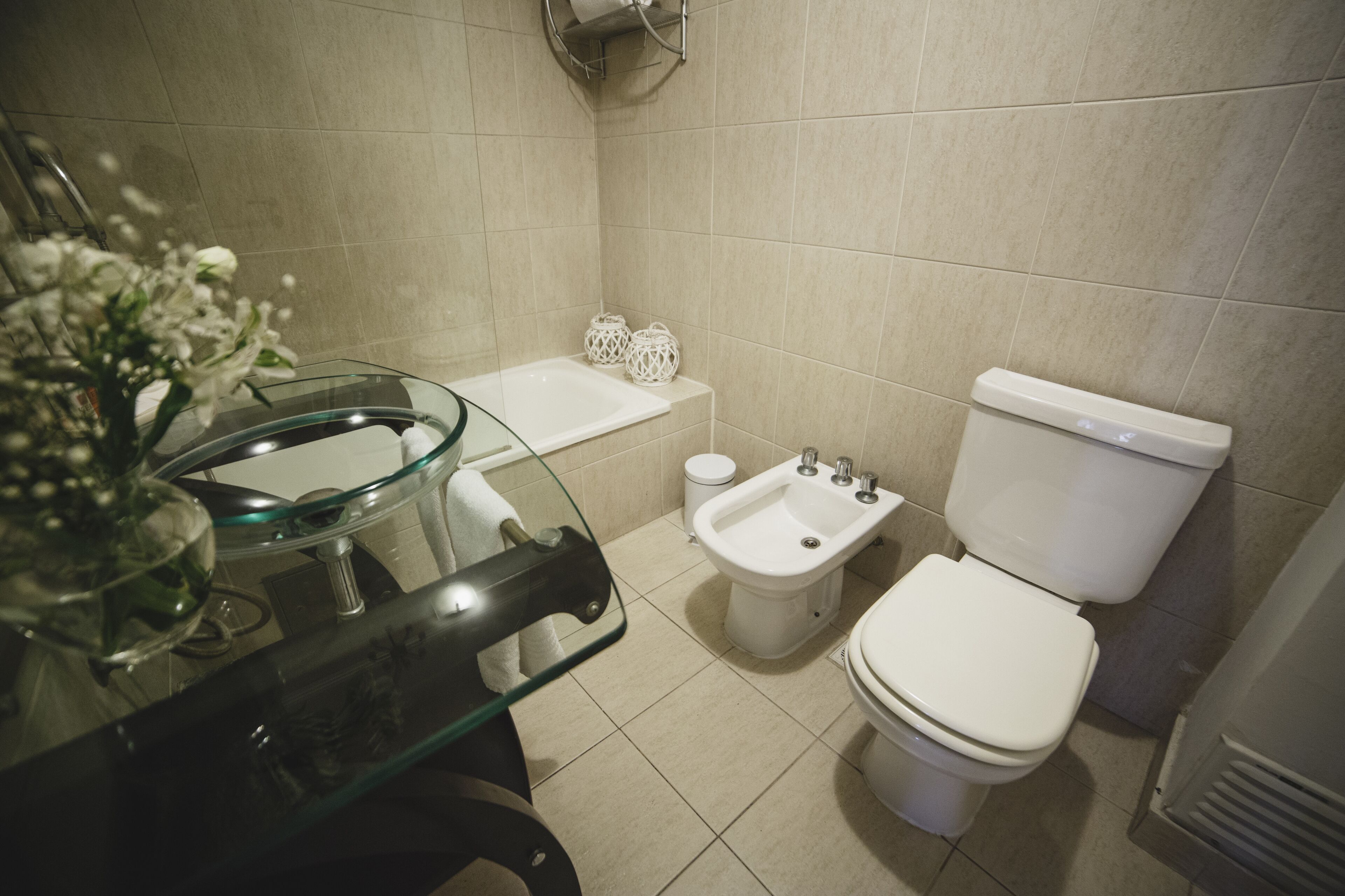 A modern bathroom with a glass sink, bidet, toilet, and a small bathtub.