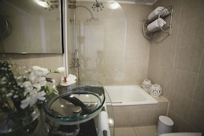 Un baño con ducha de vidrio, bañera, inodoro y lavamanos de vidrio.