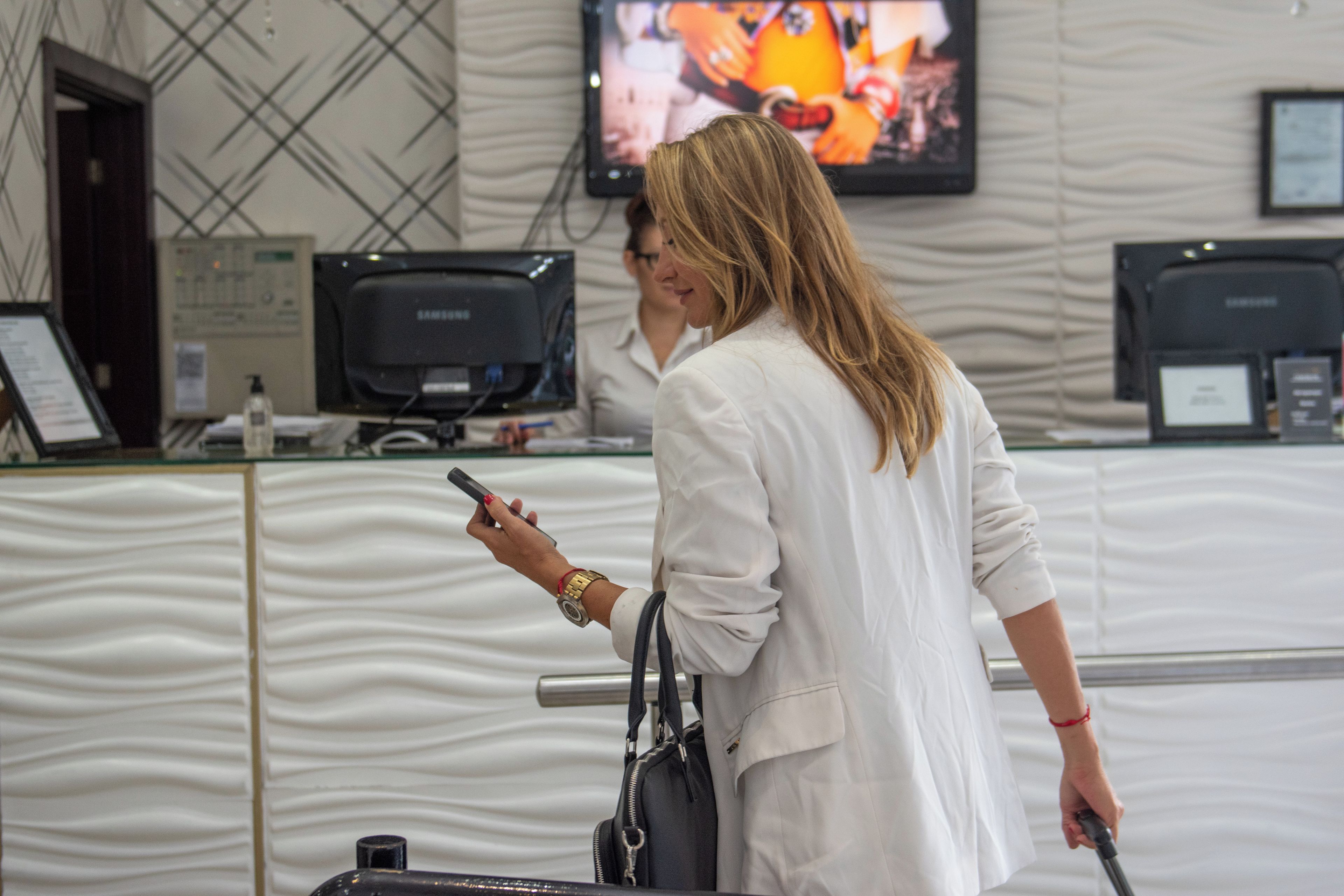 Una persona de pie frente a una mesa de recepción con un monitor de computadora, un televisor montado en la pared y un diseño de pared con motivos.