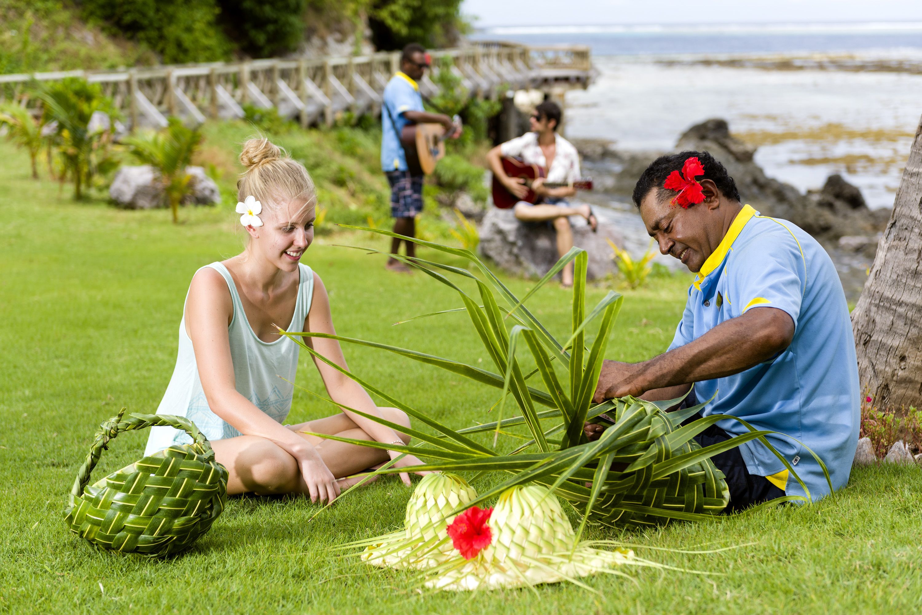 A grassy outdoor area with people engaged in activities, a wooden structure in the background, and a body of water.