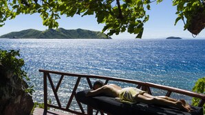 A person lying on a bench overlooking a body of water with hills in the distance. - Matamanoa Island Resort (Matamanoa Island)