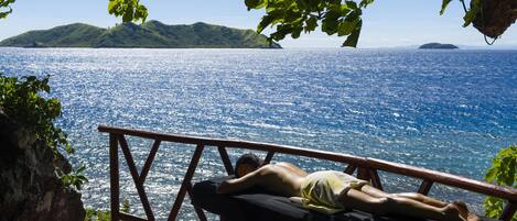 A person lying on a bench overlooking a body of water with hills in the distance.