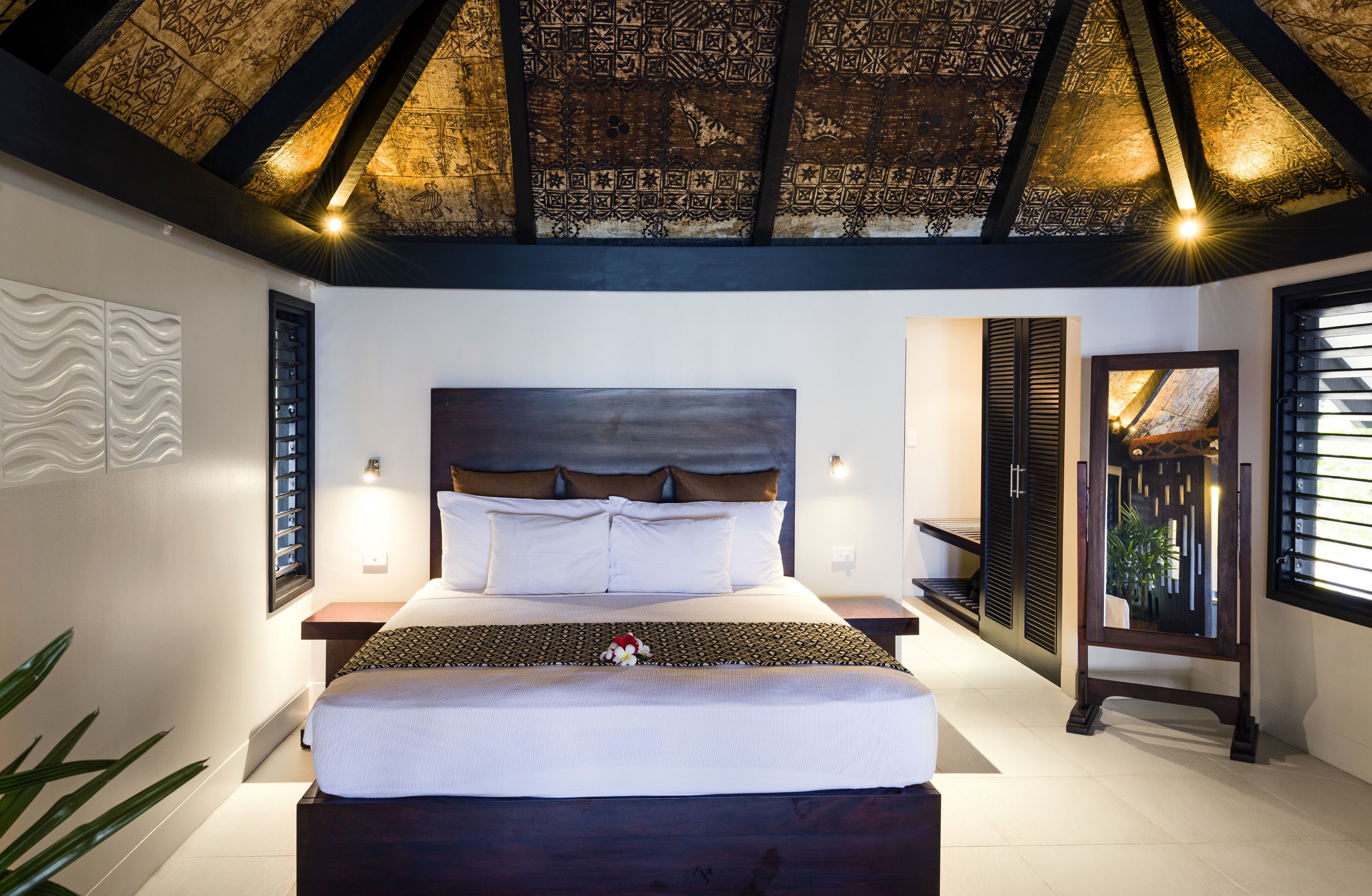 A bedroom with a large bed, a wooden ceiling, and a nightstand with a lamp.