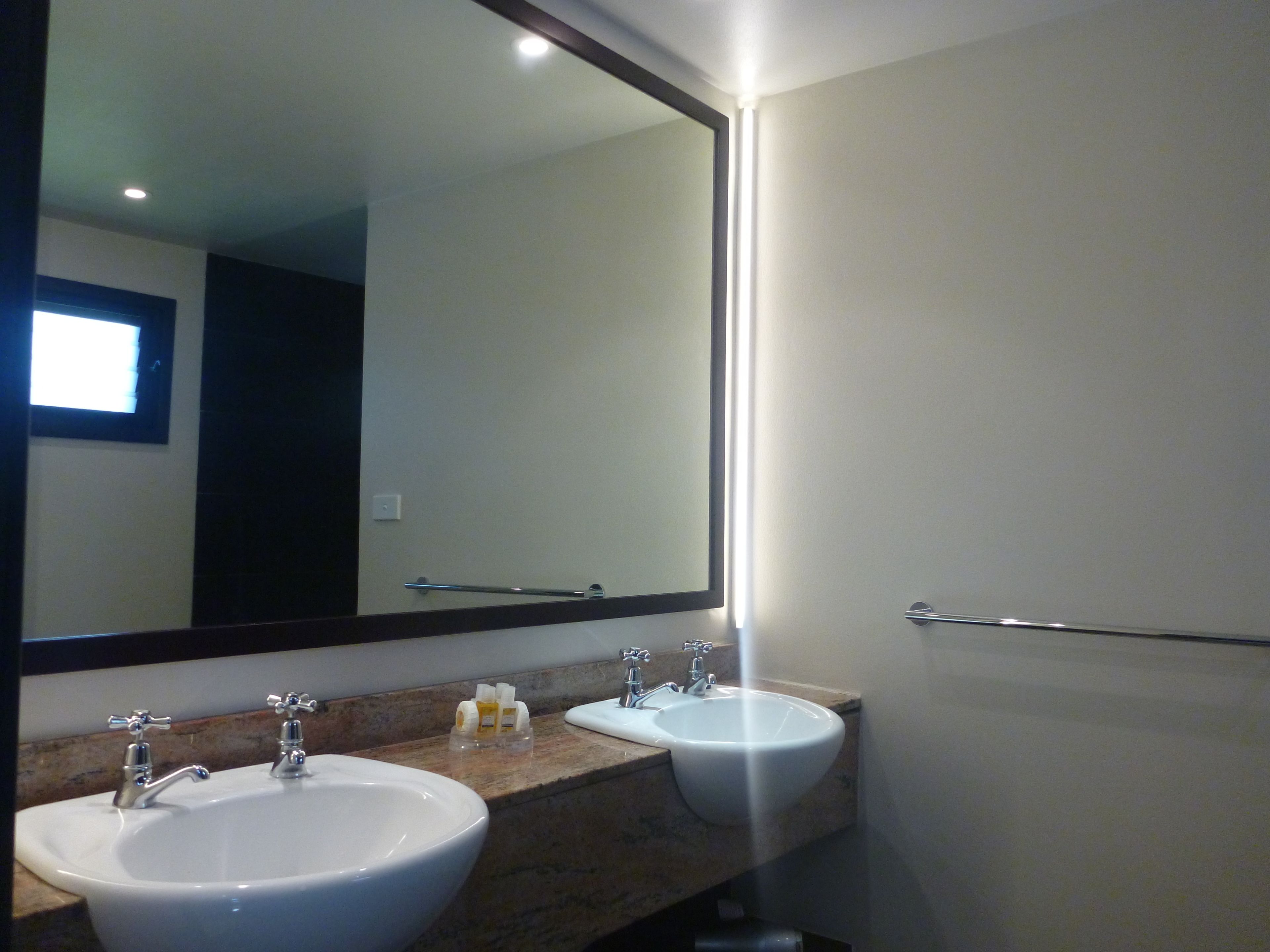 Un baño con dos lavamanos, un espejo grande y un perchero para toallas.