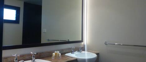 Un baño con dos lavamanos, un espejo grande y un perchero para toallas.
