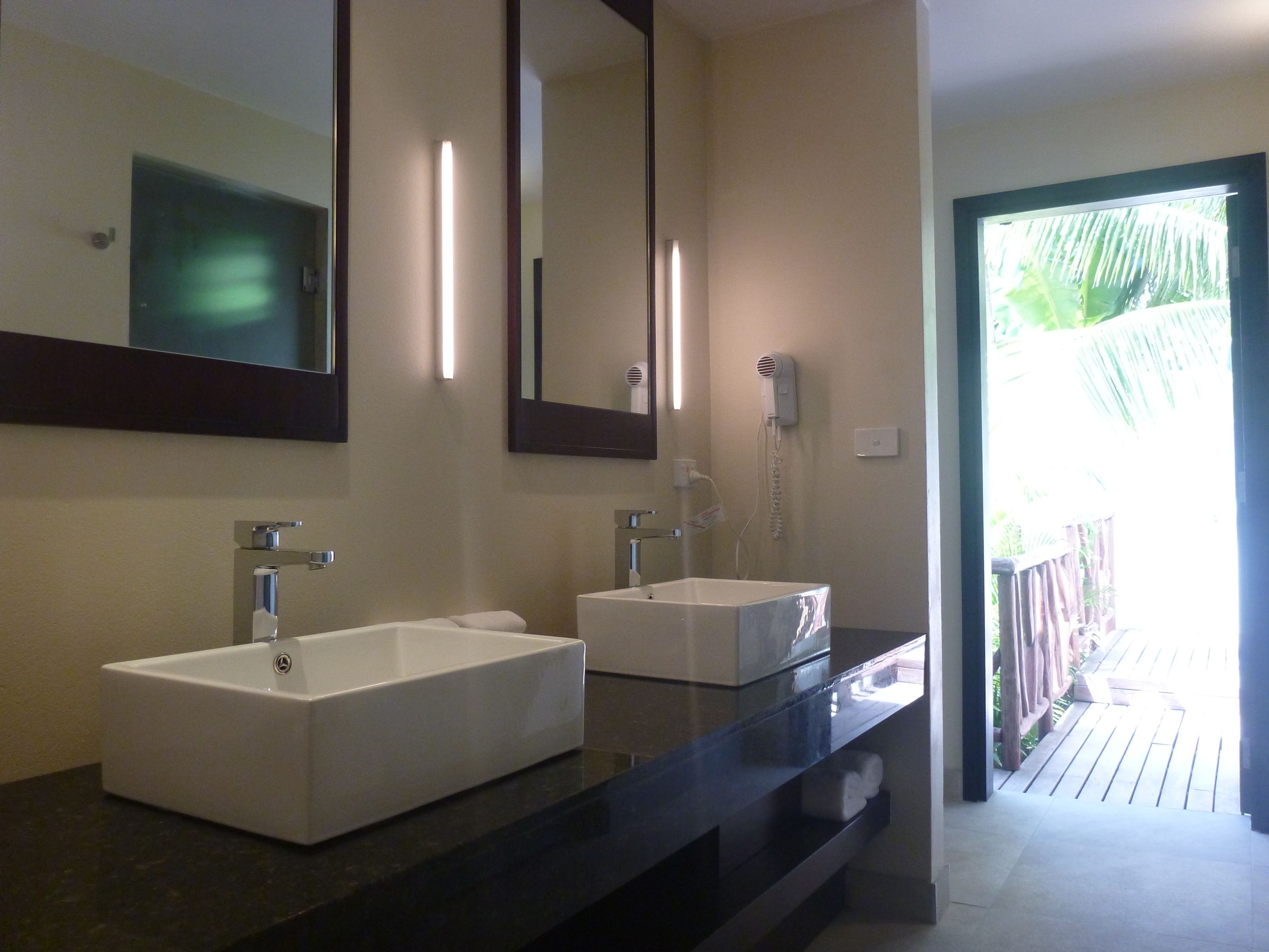 Un baño moderno con dos lavamanos blancos, un espejo grande y un secador de pelo montado en la pared.