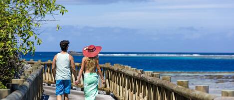 A wooden boardwalk leading to the ocean with a railing on one side.