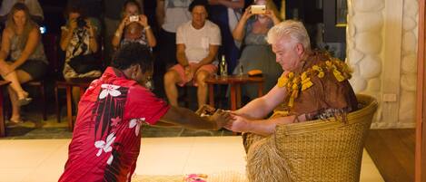 A person in a red floral shirt performing a traditional dance in front of an audience seated on chairs.
