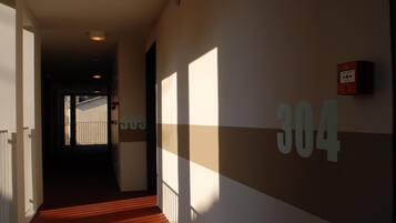 A hallway with a number 304 sign on the wall, a fire alarm, and a view of a building outside.