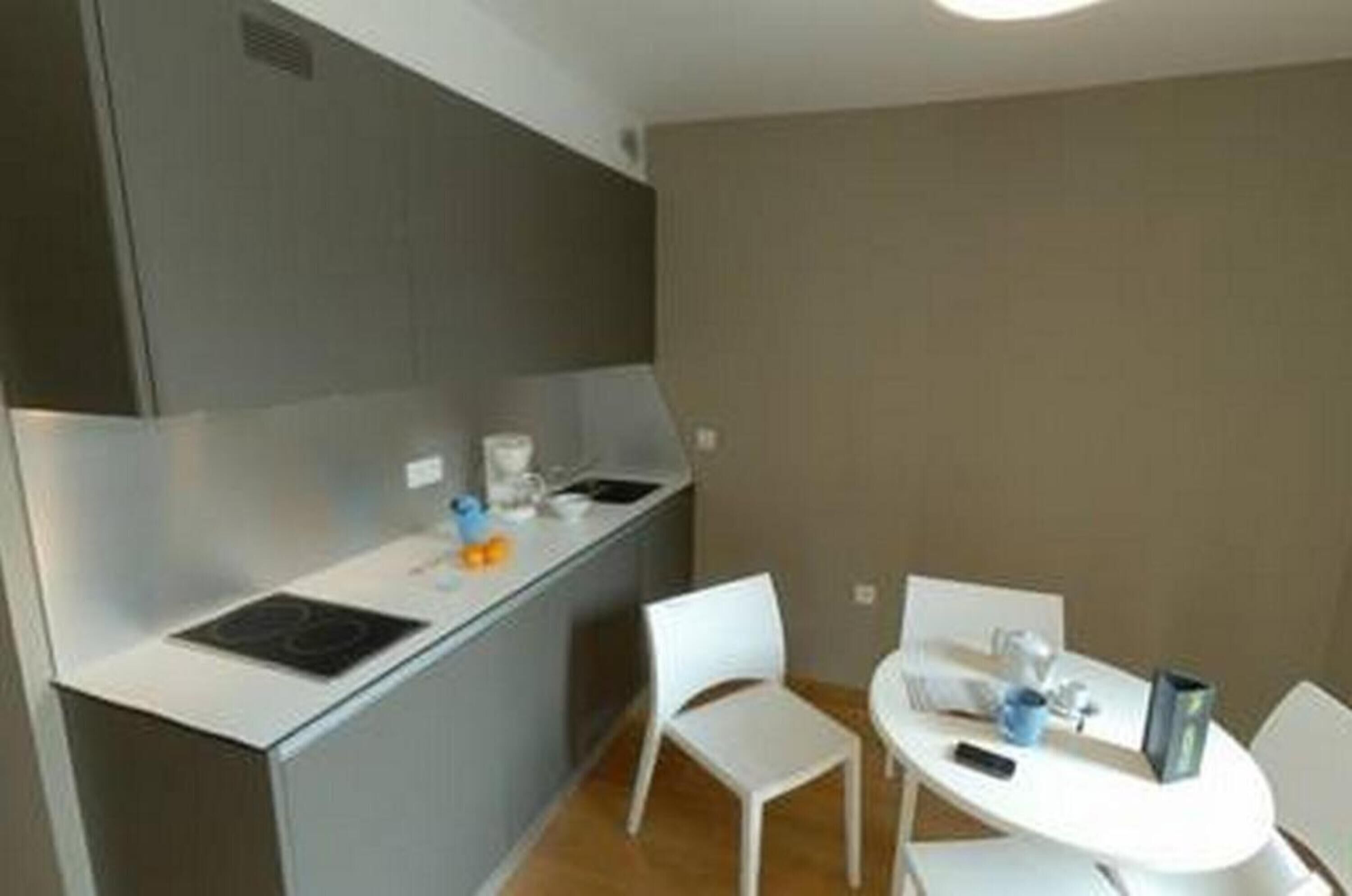 Una cocina compacta con cubierta blanca, estufa integrada y un pequeño comedor con mesa y sillas blancas.