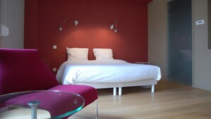 Un dormitorio moderno con cama, una mesita de vidrio y una silla roja.