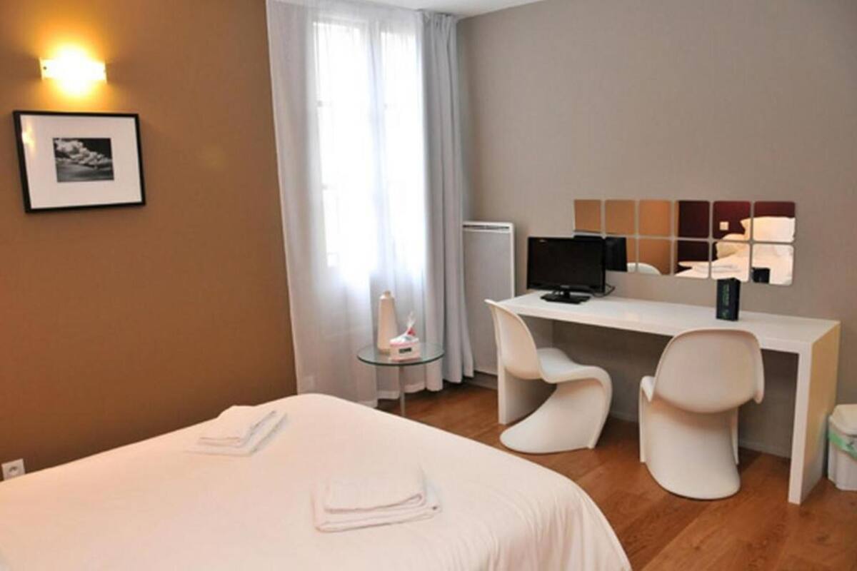 Une chambre d’hôtel avec un lit, un bureau avec un ordinateur, une chaise et une petite table avec une lampe.