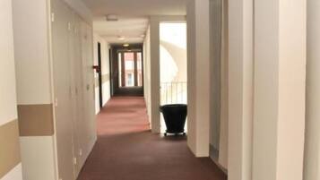 A long, narrow hallway with a red carpet, white walls, and a black trash bin at the end.