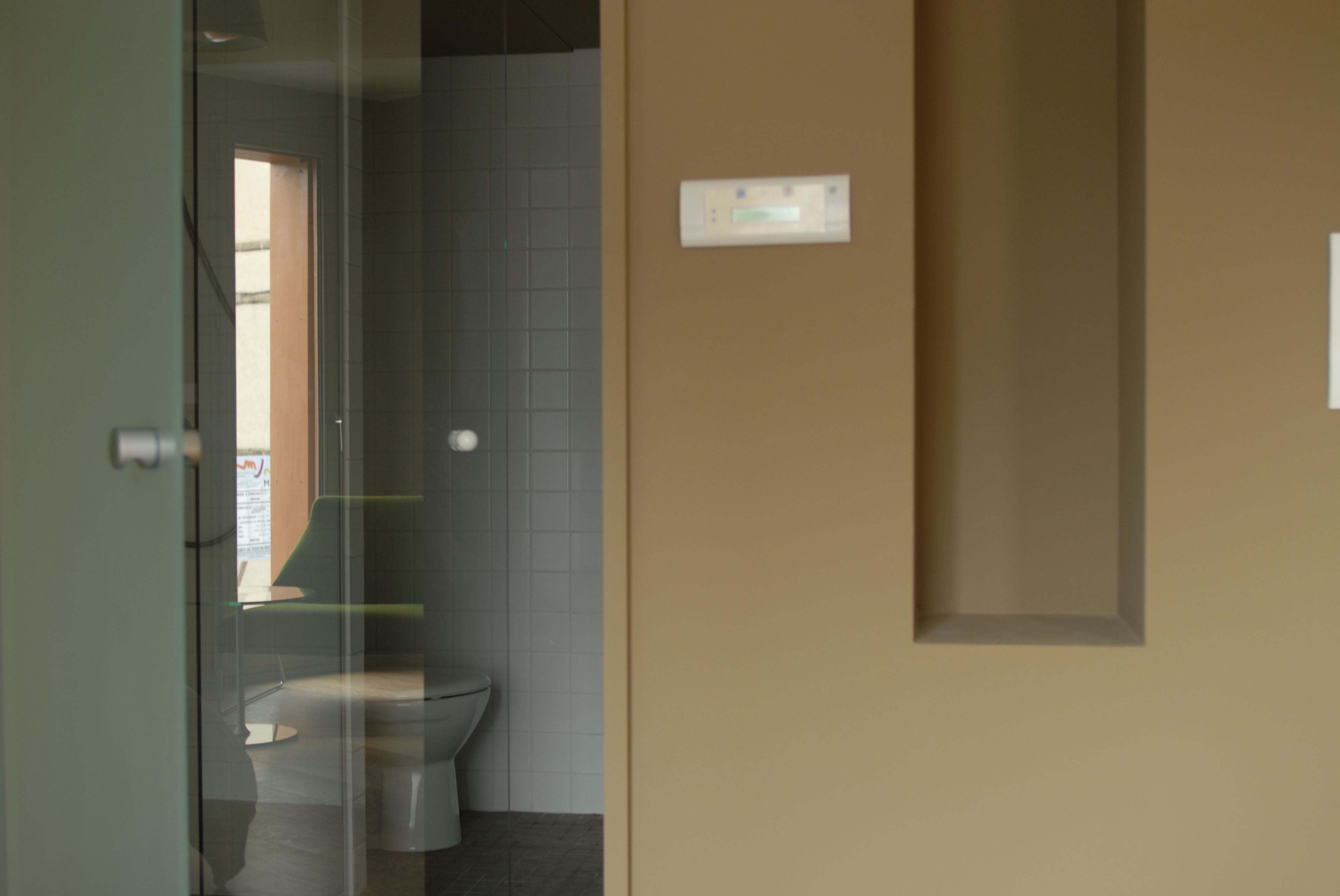 Une salle de bain équipée de toilettes, d’une paroi en verre et d’un thermostat fixé au mur.