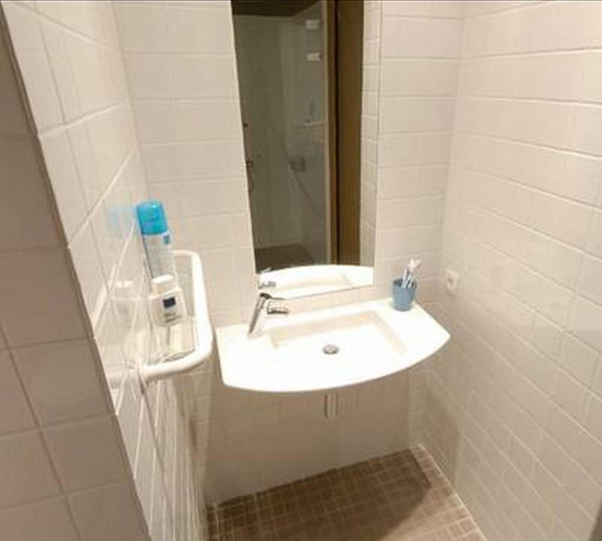 Un baño pequeño con lavamanos blanco, espejo y un perchero para toallas.