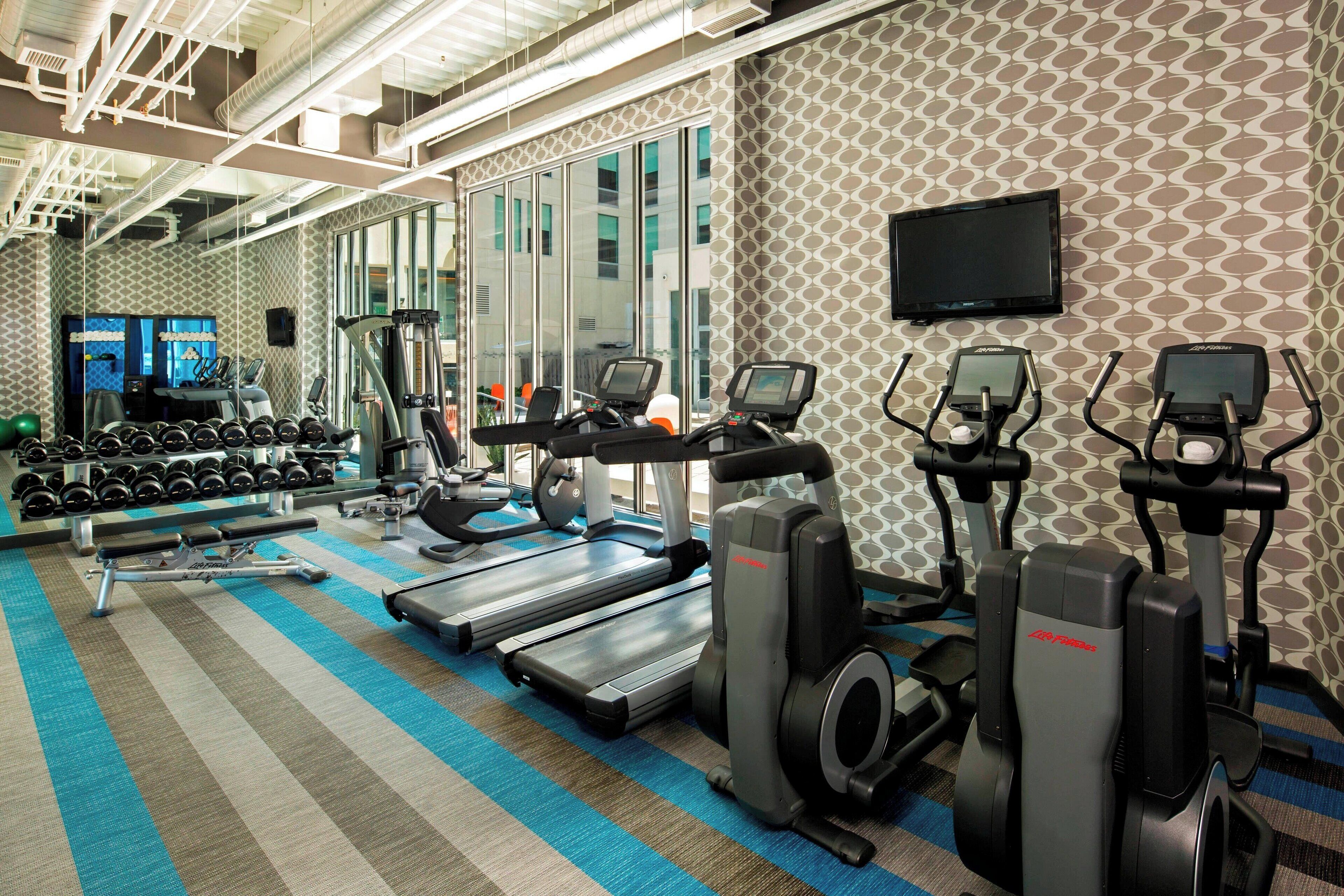 A gym with treadmills, elliptical machines, and dumbbells.