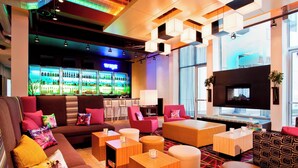 A modern lounge area with sofas, tables, and a bar with illuminated shelves. - Aloft by Marriott Milwaukee Downtown (Milwaukee)