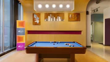 A pool table in a room with wooden paneling, a cityscape artwork, and a sign for Alloft Hotels.