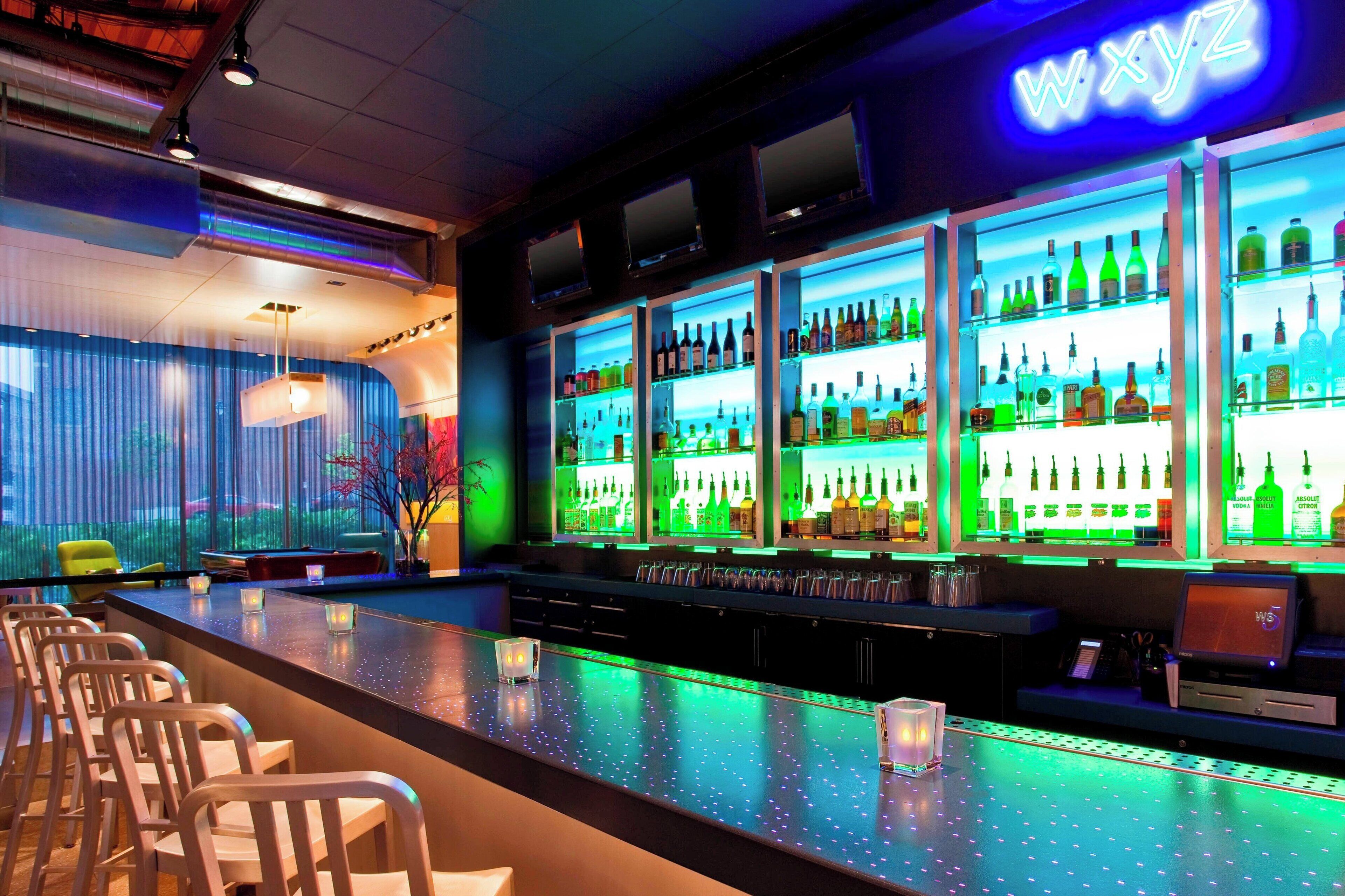 Un espace bar agrémenté d'un néon, de nombreuses étagères remplies de bouteilles et de tabourets de bar.