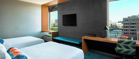 A hotel room with two beds, a desk, a chair, a TV, and a window with a city view.