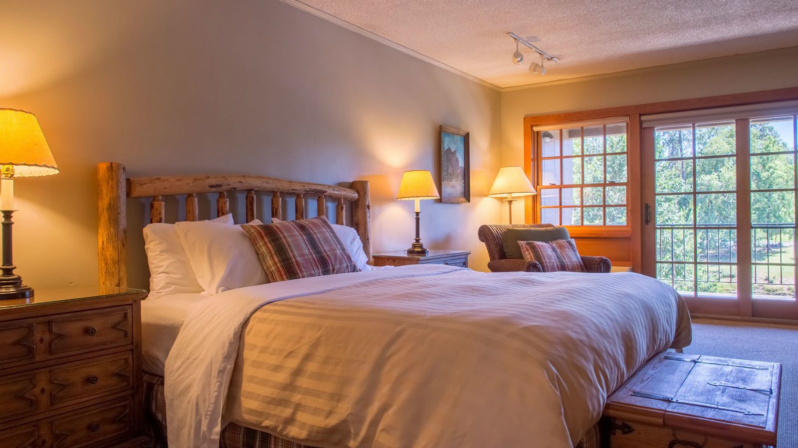 A bedroom with a large bed, two bedside tables, a chair, and a window with a view of trees.