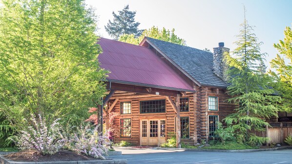 A log cabin with a red roof, wooden exterior, and a stone chimney.