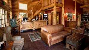 A log cabin interior with a leather sofa, wooden furniture, a staircase, and a bar area. - The Lodge at Riverside (Grants Pass)