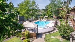 A swimming pool with a wooden deck, surrounded by trees and a view of a river.