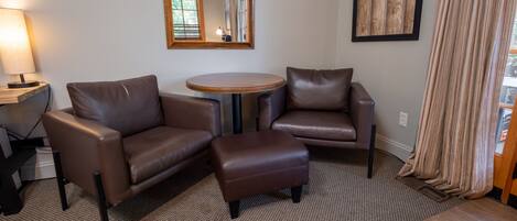 A modern living room with two leather sofas, a small round table, a lamp, and a large mirror on the wall.